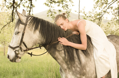 Schöne junge Frau reitet Pferd, trägt weißes Sommerkleid, lizenzfreies Stockfoto