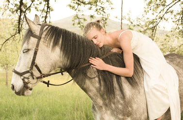 Schöne junge Frau reitet Pferd, trägt weißes Sommerkleid - FCF01396