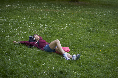 Junge Frau liegt auf einer Wiese und hört Musik mit Kopfhörern und Mobiltelefon, lizenzfreies Stockfoto