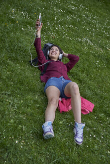 Junge Frau liegt auf einer Wiese und hört Musik mit Kopfhörern und Mobiltelefon - BEF00094