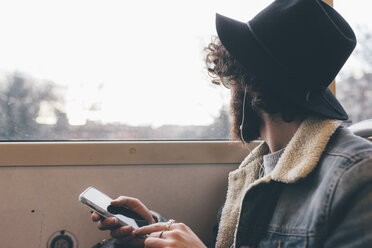 Junger Mann sitzt in der U-Bahn, hält sein Smartphone und schaut aus dem Fenster - CUF11419