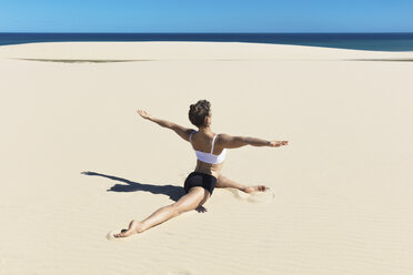 Rückansicht einer Frau am Strand, die einen Spagat macht, mit geöffneten Armen in Yoga-Position - CUF11444