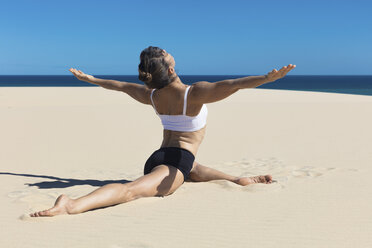 Rückansicht einer Frau am Strand, die einen Spagat macht, mit geöffneten Armen in Yoga-Position - CUF11445