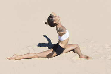 Seitenansicht einer Frau am Strand, die einen Spagat macht, Arme in Yoga-Position geöffnet - CUF11446