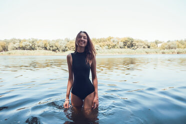 Porträt einer Frau im Badeanzug, die im Wasser steht und lächelnd in die Kamera schaut - CUF11449
