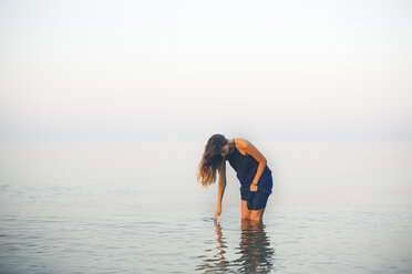 Young woman knee deep in sea touching surface, Odessa, Ukraine - CUF11474