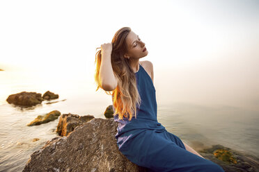 Junge Frau auf einem Felsen am Strand sitzend mit der Hand im langen Haar, Odessa, Ukraine - CUF11476