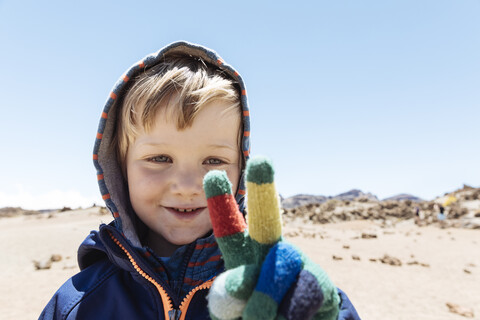 Porträt eines niedlichen Jungen, der mit seiner behandschuhten Hand auf dem Berg Teide, Teneriffa, Kanarische Inseln, ein Friedenszeichen macht, lizenzfreies Stockfoto