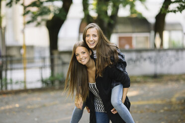 Portrait of young woman giving best friend a piggy back in park - CUF11507