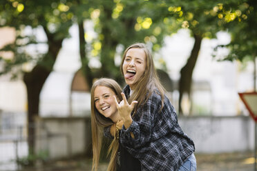 Portrait of young woman giving friend piggy back in park - CUF11508