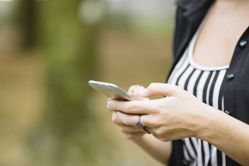 Ausgeschnittene Aufnahme einer jungen Frau, die im Park den Touchscreen eines Smartphones benutzt - CUF11510