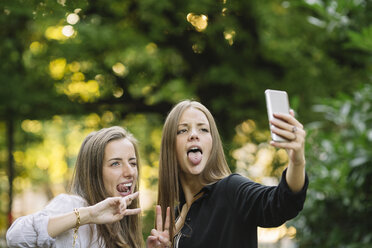 Zwei junge Freundinnen ziehen Grimassen für ein Smartphone-Selfie im Park - CUF11515