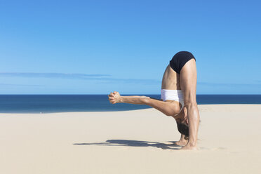 Seitenansicht einer Frau am Strand, die sich in Yoga-Position nach vorne beugt - CUF11528