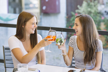 Two young female friends raising a cocktail toast at sidewalk cafe - CUF11558