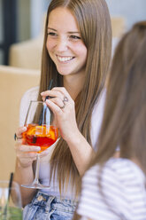 Blick über die Schulter auf zwei junge Freundinnen, die in einem Straßencafé Cocktails trinken - CUF11559