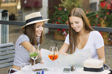 Two young female friends looking at map at sidewalk cafe - CUF11560