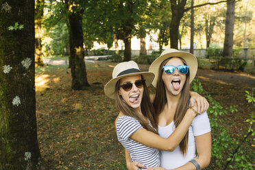 Portrait of two young female friends in trilby hats sticking out tongues in park - CUF11561