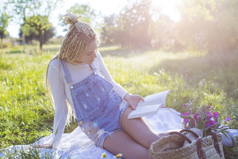 Junge Frau liest ein Buch auf einer Picknickdecke in einem Feld, Mallorca, Spanien - CUF11807