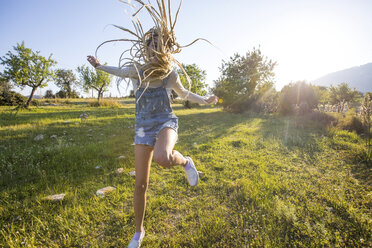 Fröhliche junge Frau mit langem geflochtenem blondem Haar, die vor Freude auf einem Feld springt, Mallorca, Spanien - CUF11811