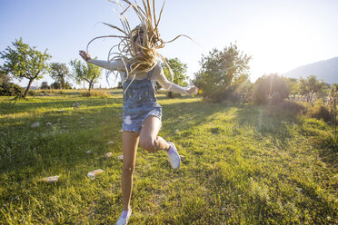 Fun young woman with long plaited blond hair jumping for joy in field, Majorca, Spain - CUF11811