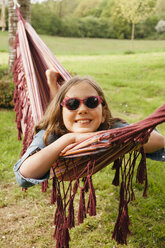 Portrait of smiling girl wearing sunglasses lying in hammock - ANHF00045