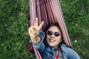 Smiling girl wearing sunglasses lying in hammock showing victory sign - ANHF00048