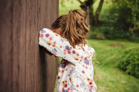 Mädchen lehnt an einer Holzwand und versteckt ihr Gesicht, lizenzfreies Stockfoto