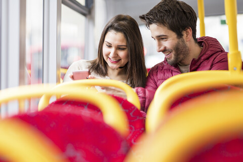 UK, London, glückliches junges Paar im Bus, das auf sein Handy schaut, lizenzfreies Stockfoto