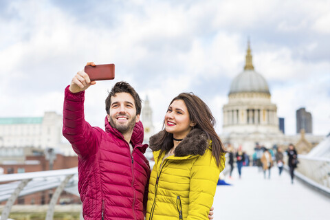 UK, London, Porträt eines lächelnden jungen Paares, das ein Selfie mit seinem Handy vor der St. Pauls Cathedral macht, lizenzfreies Stockfoto