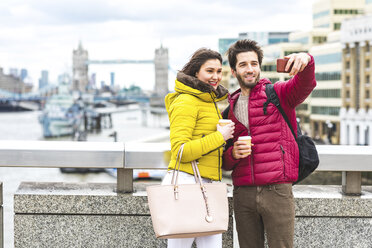 UK, London, junges Paar mit Kaffee zum Mitnehmen steht auf der Brücke über die Themse und macht ein Selfie mit Smartphone - WPEF00283