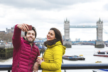 Großbritannien, London, junges Paar steht auf einer Brücke über die Themse und macht ein Selfie mit Smartphone - WPEF00285