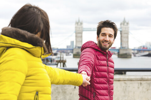 UK, London, portrait of smiling young man standing hand in hand on bridge over the Thames with his girlfriend stock photo