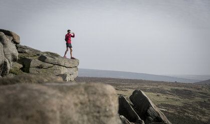 Männlicher Läufer beim Fotografieren vom Gipfel des Stanage Edge, Peak District, Derbyshire, Großbritannien - CUF11867