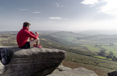 Männlicher Läufer, sitzend, mit Blick von der Spitze des Stanage Edge, Peak District, Derbyshire, UK - CUF11868
