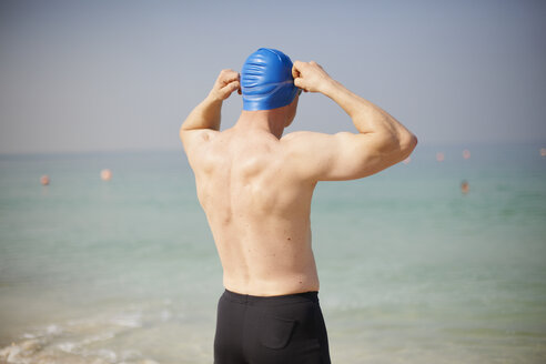 Rückansicht eines reifen Mannes, der seine Badekappe am Strand anpasst, Dubai, Vereinigte Arabische Emirate - CUF11873