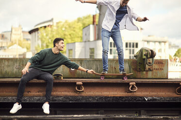 Two young men fooling around by train track, balancing on skateboard Bristol, UK - CUF11887