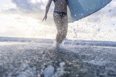 Neck down view of woman carrying surfboard and splashing in sea, Nosara, Guanacaste Province, Costa Rica - CUF11892