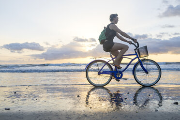 Frau beim Radfahren am Strand bei Sonnenuntergang, Nosara, Provinz Guanacaste, Costa Rica - CUF11893