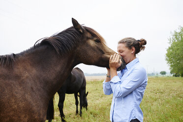 Frau mit Gesicht an der Schnauze eines Pferdes auf einem Feld - CUF11913