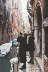 Paar fotografiert Gebäudefassaden vom Kanalufer aus, Venedig, Italien - CUF11924