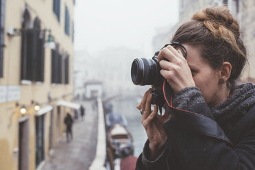 Young woman photographing on misty canal waterfront, Venice, Italy - CUF11928