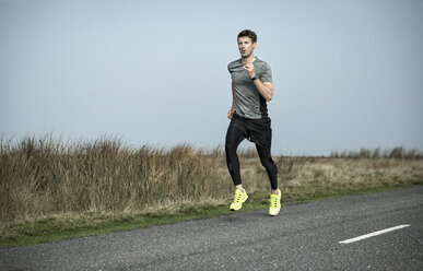 Male runner running along rural moorland road - CUF11947
