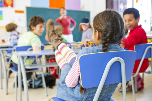 Rückansicht einer Grundschülerin mit Füßen auf dem Schreibtisch im Klassenzimmer - CUF11976