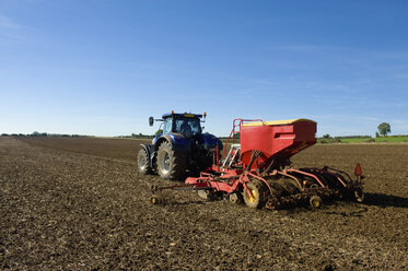 Rückansicht eines Landwirts, der einen Traktor mit Sämaschine auf einem gepflügten Feld im Frühjahr fährt - CUF11993