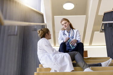 Zwei Ärztinnen machen eine Pause im Treppenhaus eines Krankenhauses und unterhalten sich - CUF11999