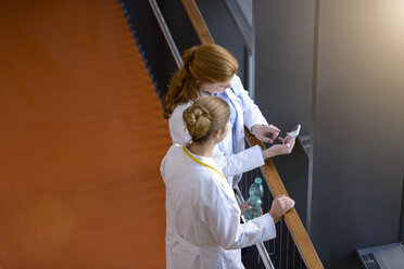 Blick von oben auf zwei Ärztinnen auf dem Krankenhausbalkon, die auf ihr Smartphone schauen - CUF12002