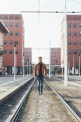 Cool young bearded man walking along city tram lines - CUF12029