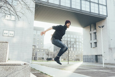 Junger männlicher Hipster springt mitten in der Luft und übt Parkour in der Stadt - CUF12040