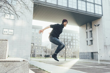Young male hipster jumping mid air practicing parkour in city - CUF12040