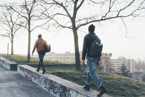 Rückansicht von zwei jungen männlichen Hipstern, die an einer Parkmauer entlanggehen - CUF12044